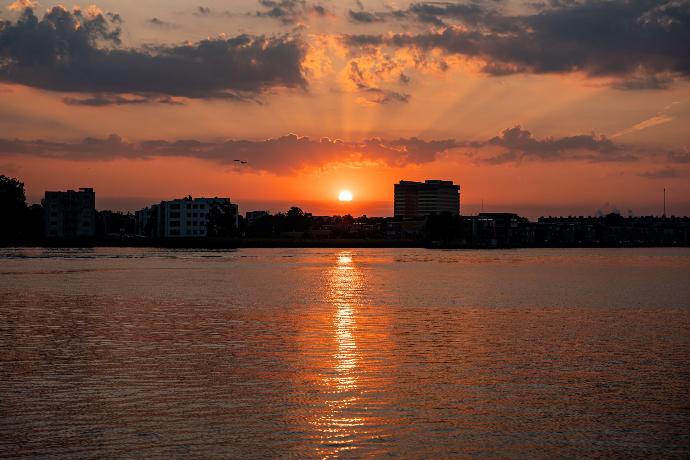 a body of water with buildings and a sunset in the background